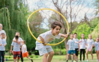 a young boy holding a yellow hula hoop in front of a group of people